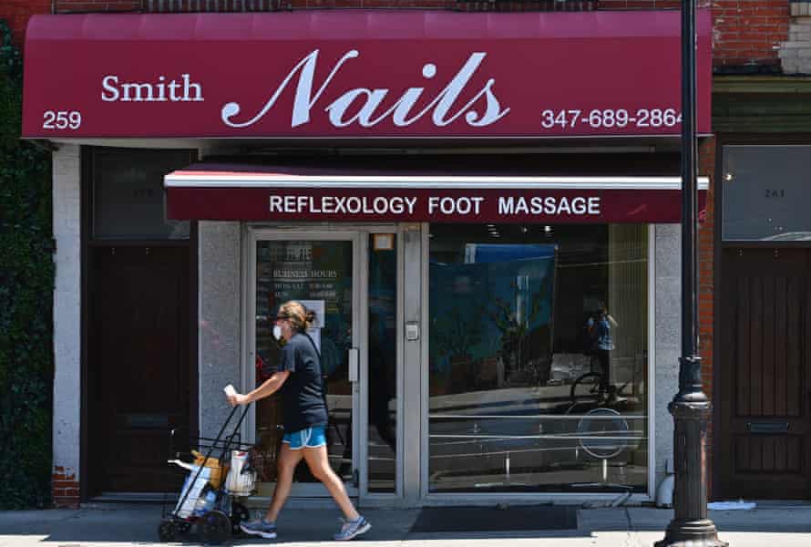 A woman pushes a cart past a storefront with a sign above it that reads “Smith Nails”.
