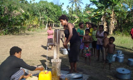 People line up to collect water in plastic containers and cooking pots from a communal pump in a rural community in Madang Province, Papua New Guinea.