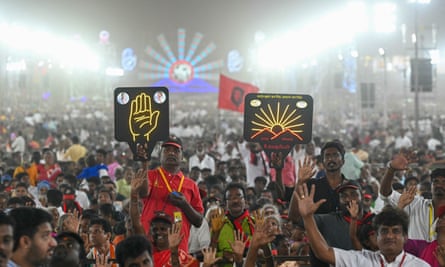 A huge crowd of people, some with arms in the air and two holding signs: one of the palm of a hand, and one of a sun rising between two mountains