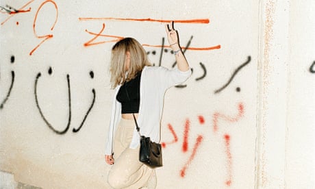 A young woman with her hair out raises her hands as a sign of protest in front of graffiti that says in Farsi: “Woman, life, freedom”.