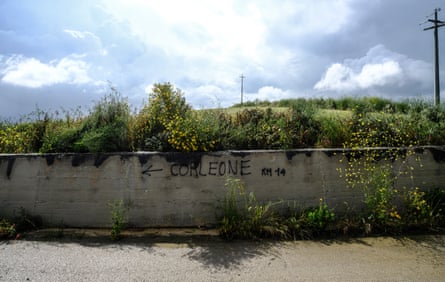 La strada da Palermo a Corleone è dissestata e spesso manca di segnaletica stradale.  Di tanto in tanto, sui muri che delimitano la campagna, cartelli stradali scritti con bombolette spray indicano la strada per il paese.