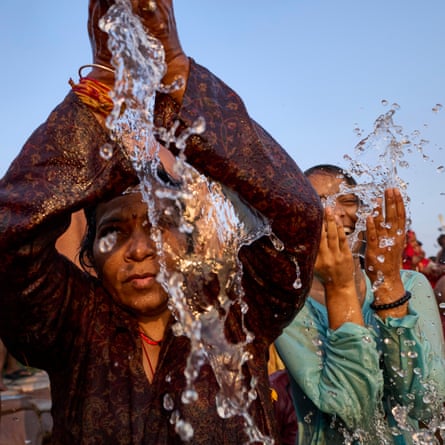 Two women in a river splash water over themselves with their cupped hands