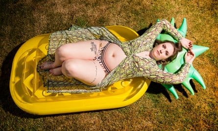 Lena Dunham photographed in Wales, July 2019, in a biki and dress, lying on a pineapple lilo