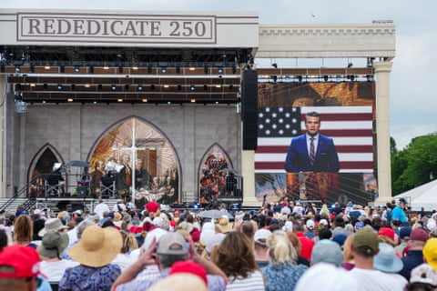 video of man in suit in front of american flag plays on screen in front of crowd outside