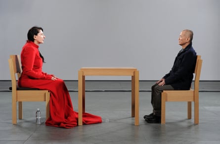 Abramović in red dress sits across wooden table from man in black