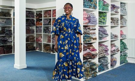 Yvonne Telford wearing a full-length blue-patterned dress, pictured in her warehouse with shelves of her clothing behind her