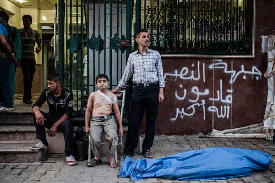 ‘His father had gone, and he didn’t quite understand that’ … Ahmed, 12, waits with his uncle by the body of his father who was killed by a shell in Aleppo, Syria. Ahmed was also injured in the back by shrapnel.