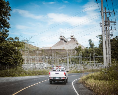 A white van drives on a road past a large open pit mine