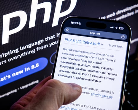 A hand holds a smartphone showing a PHP security update, with the PHP website blurred behind