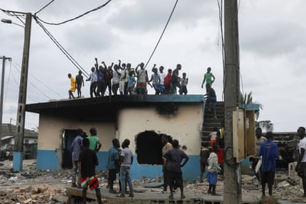 People stand on the roof of a police station set on fire by protesters during a demonstration against the decision of Ivory Coast President Alassane Ouattara to run for a third term in the next presidential election, in Bonoua, Ivory Coast, on 14 August.