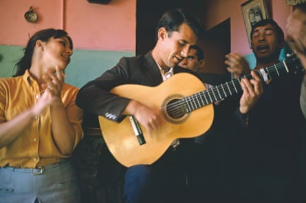 Man playing a guitar in a bar with people clapping.
