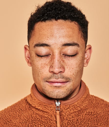 Loyle Carner in an orange fleece top, zipped up, and with his eyes closed.