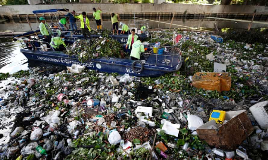 Municipal garbage collectors in boats try to clear a canal of floating debris and household waste