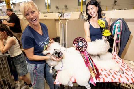 Two women laugh with a lazing poodle in a booth; one is fanning him