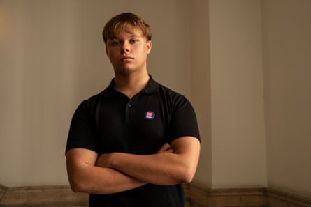 Adam Dragan with his arms crossed wearing a black polo shirt in a corridor at KCL
