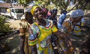 A woman wearing a dress bearing the face of Robert Mugabe joins with others to sing political songs in his home village of Kutama