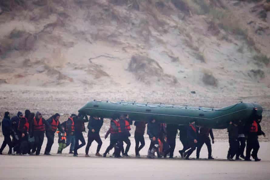 A group of migrants run on the beach with an inflatable dinghy near Wimereux, France