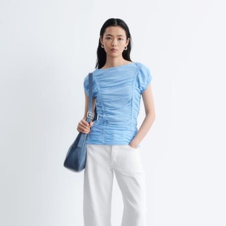 A model wears a baby blue &Other Stories Ruched Cap-Sleeve Top wih white trousers.
