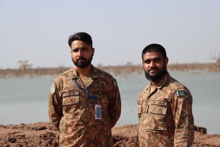 Two men in military fatigues stand in front of a body of water.