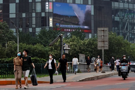 People walking past a screen broadcasting a news report in Beijing.
