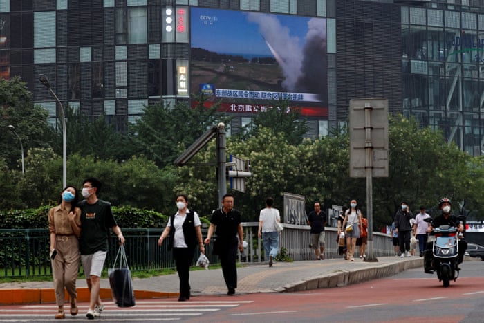 People walking past a screen broadcasting a news report in Beijing.