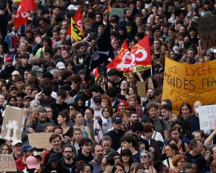A large protest, the frame filled with people, some of them carrying flags and banners