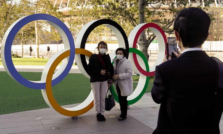 Visitors wearing face masks take a photo at the Olympic Rings monument in front of the Japan Olympic Committee headquarters in Tokyo