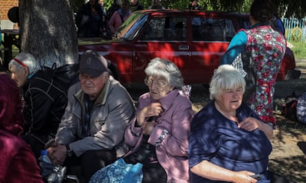 Older people sit on a bench with their belongings around them