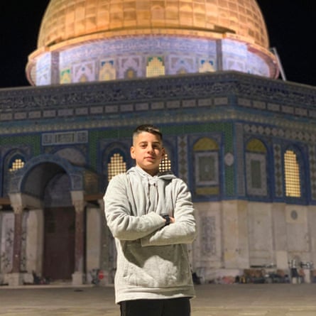 a young boy stands with his arms crossed in front of al-Aqsa mosque
