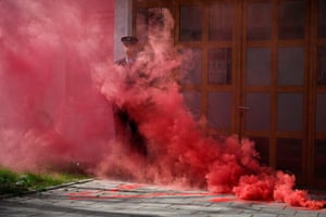 A police officer stands amid red smoke from a flare in a doorway