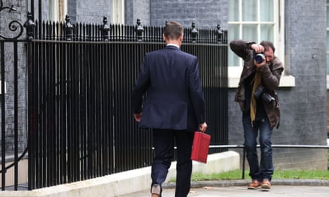 A photographer is taking a photo of Jeremy Hunt, who is walking away from us down Downing Street holding his red box