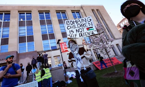 people in front of a building, one with sign saying 'bombing children is not self defense'