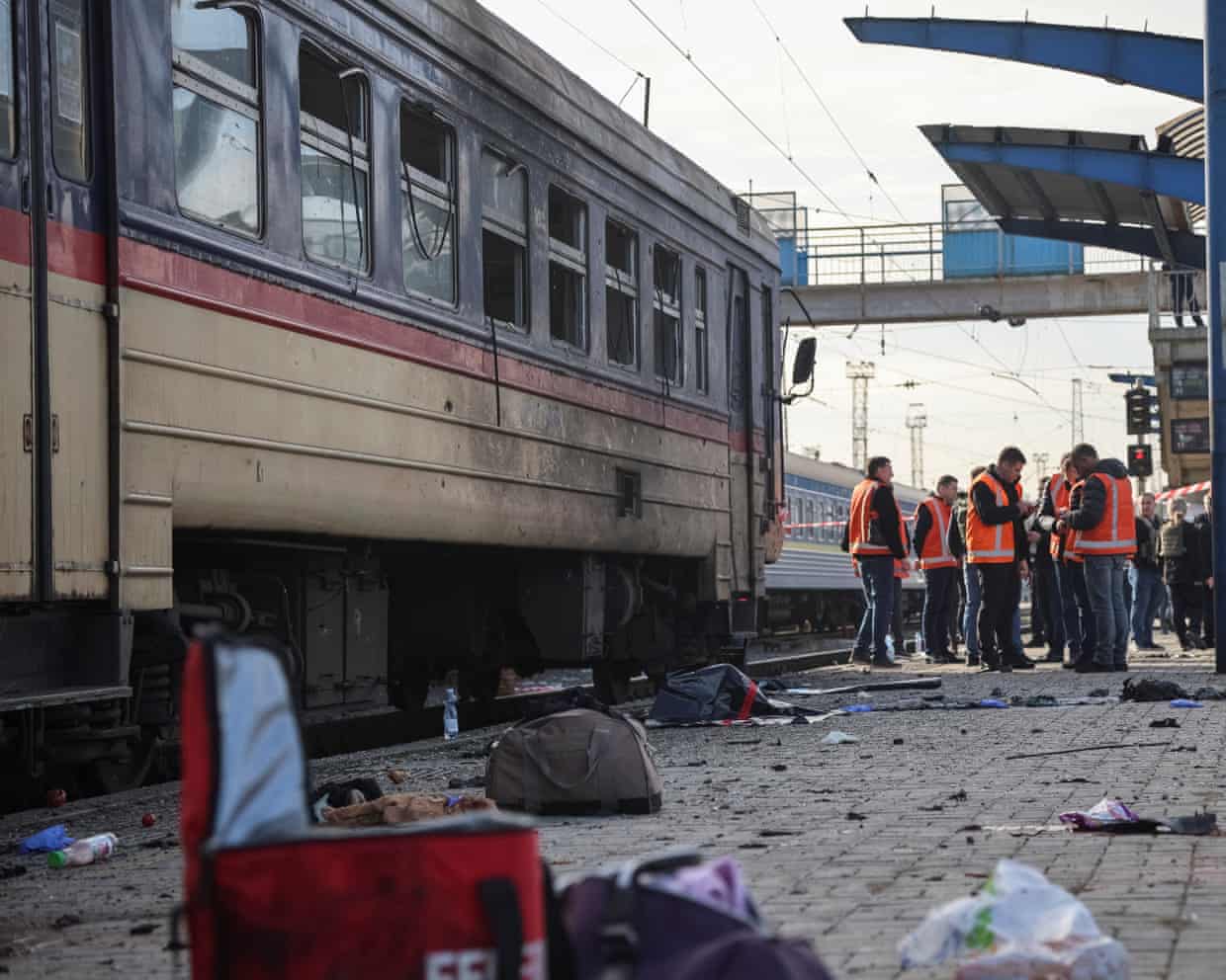 Emergency workers inspect a train damaged in a drone strike, debris scattered on the platform.