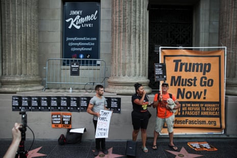 People standing outside the theatre with a large banner saying Trump Must Go Now!