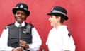 British ConstablesLondon, England - May 5th, 2008: Two female constables surveying a city market along the street. They are talking in front of a red wall. Police is needed to keep crowds in order and prevent theft.
