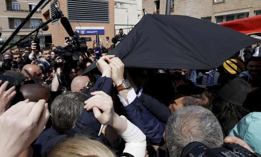 Foule de personnes avec des micros de presse et un parapluie noir.