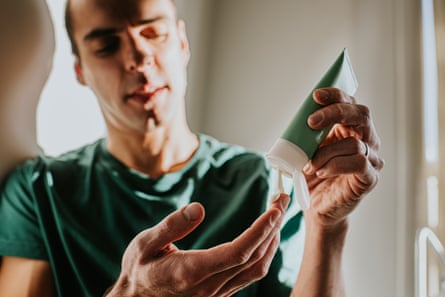 A man in a green T-shirt holds a tube of cream and squeezes the contents on to his other hand.