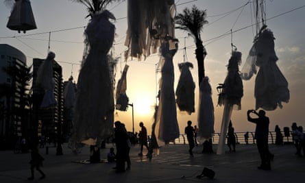 A man photographs rows of wedding dresses hanging from nooses on a Beirut beach.
