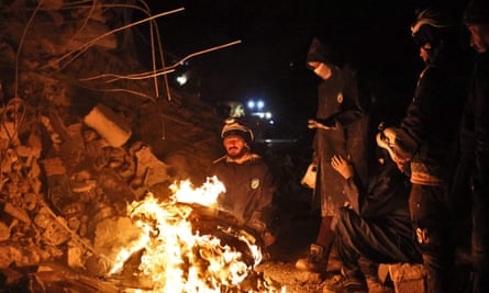 Rescue workers warm themselves by a fire next to a collapsed building in Sarmada, Idlib province.