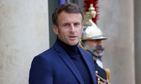 French President Emmanuel Macron, wearing a navy turtleneck jumper in front of a guard in plumed helmet and uniform at the Elysée Palace in Paris