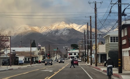 a person crosses a wide street among low buildings, with mountains in the background