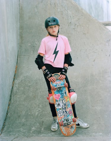 girl in helmet looks into camera holding up her colourful skateboard