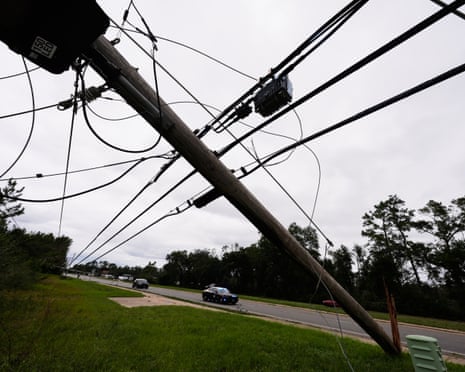 A police car drives past a severely leaning power pole after Hurricane Isaias