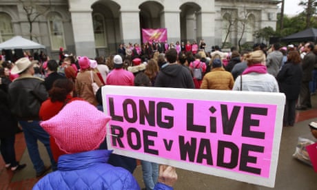 Activists gather in front of a building holding pro-choice signs. The sign in the foreground reads 'Long live Roe v Wade'.
