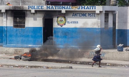 An elderly woman runs in front of the damaged police station building with tyres burning in front of it after armed gang members exchanged gunfire with police and soldiers around the airport in Port-au-Prince, Haiti on Wednesday.