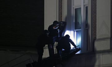 Police in riot gear break in through a window