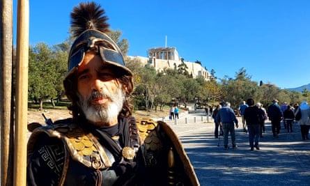 Tourists walk past a man dressed as an ancient Marathon warrior beneath the Acropolis.
