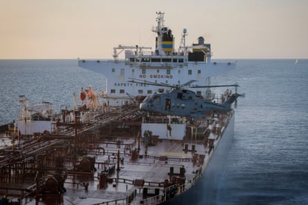 British troops descend from a hovering helicopter and stand on the deck of a huge oil tanker.