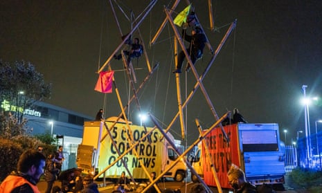 Protesters climb a bamboo scaffold between two brightly coloured vans with protest slogans on them