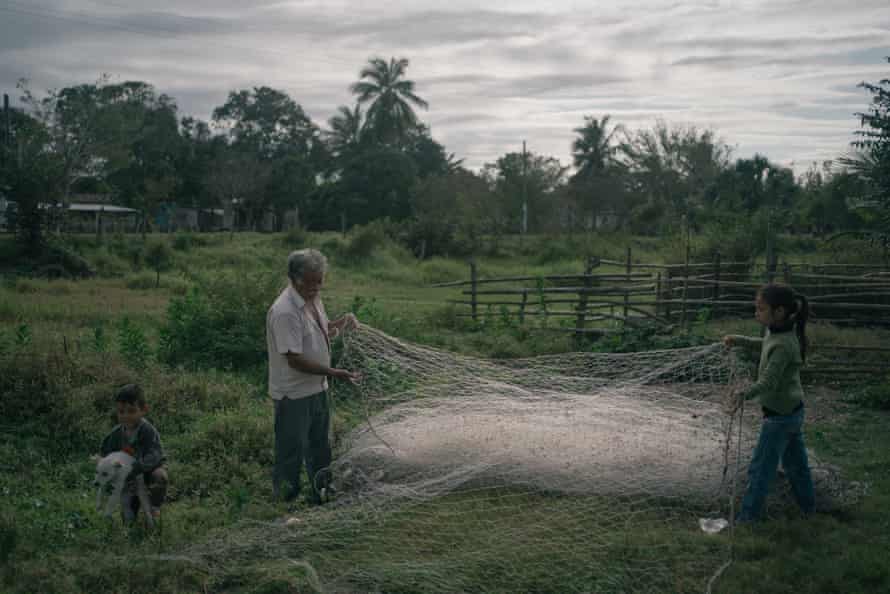 SALADERO, VERACRUZ. FEBRUARY 27: Francisco Blanco Arango untangles a fishing net with the help of his granddaughter Ada Guadalupe Blanco while Kevin Blanco Flores plays with a dog at their backyard in Saladero, Mexico.
